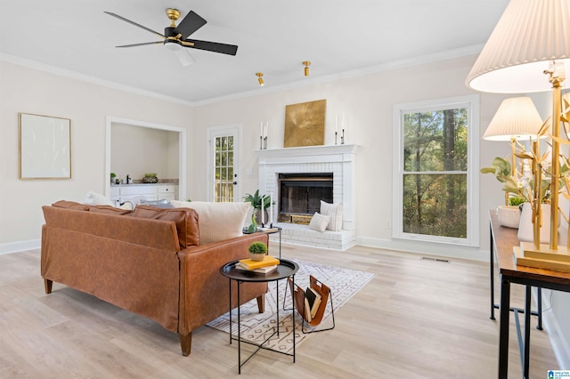 living room with crown molding, light wood-type flooring, ceiling fan, and a fireplace