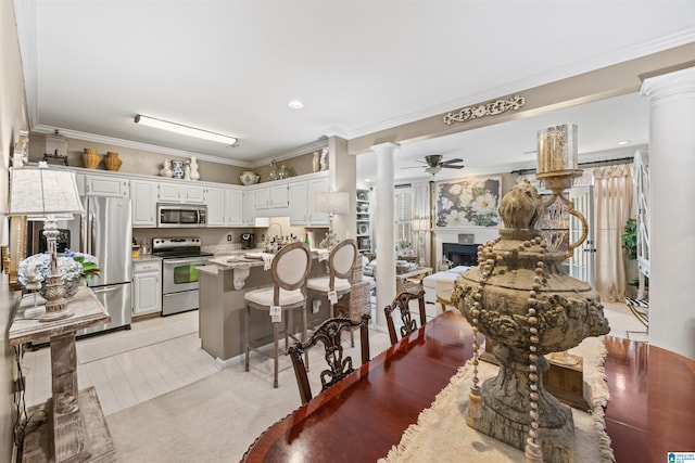 kitchen with ornate columns, appliances with stainless steel finishes, white cabinets, ornamental molding, and ceiling fan