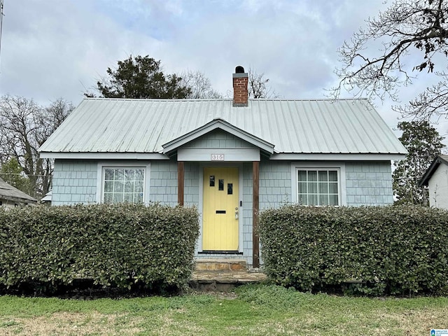 bungalow-style house with a chimney, metal roof, and a front yard