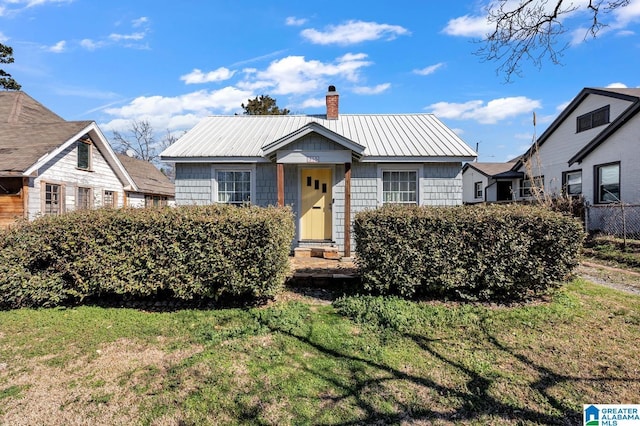 bungalow-style home with a standing seam roof, metal roof, a chimney, and a front yard