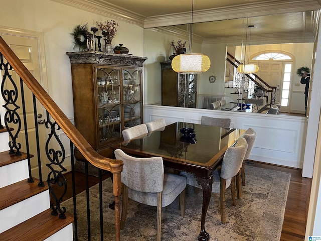 dining area with a wainscoted wall, stairway, dark wood-type flooring, crown molding, and a decorative wall