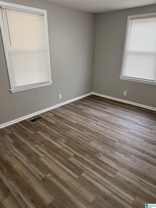 spare room featuring dark wood finished floors, visible vents, and baseboards