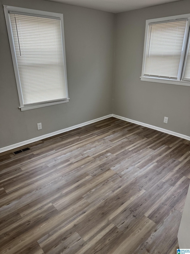 unfurnished room with wood finished floors, visible vents, and baseboards