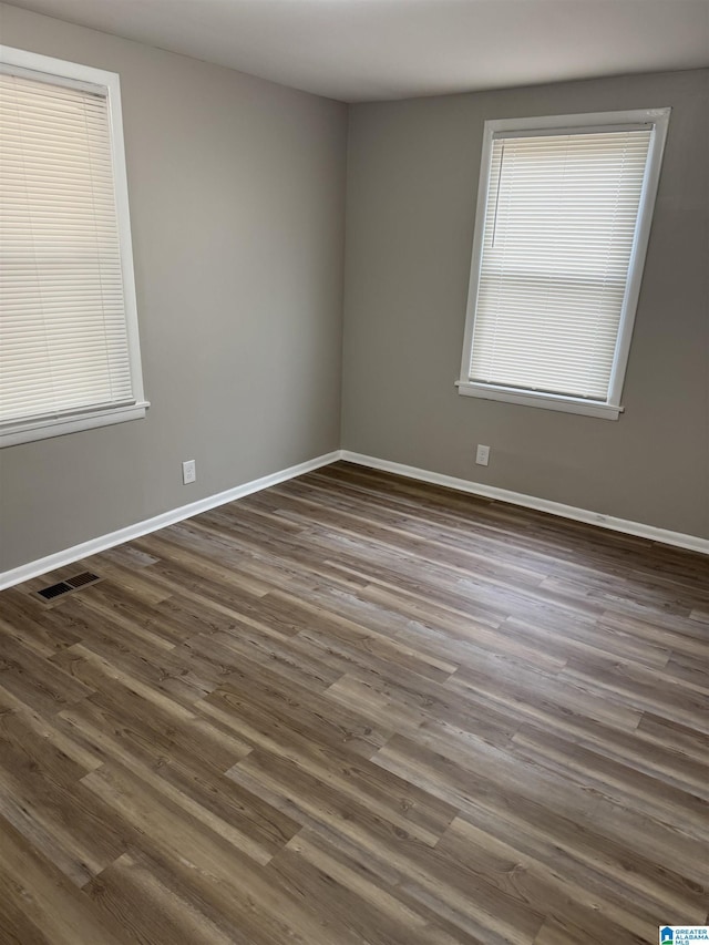 empty room featuring baseboards, visible vents, and dark wood-type flooring