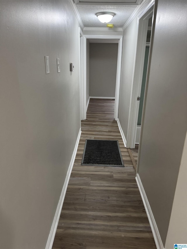 corridor with a textured ceiling, visible vents, baseboards, ornamental molding, and dark wood finished floors