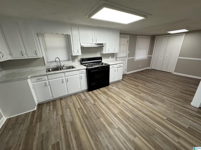 kitchen featuring light countertops, white cabinets, a sink, black gas stove, and under cabinet range hood