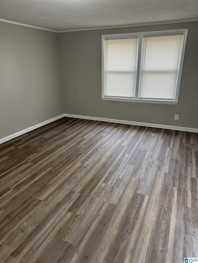 empty room with a textured ceiling, baseboards, wood finished floors, and crown molding