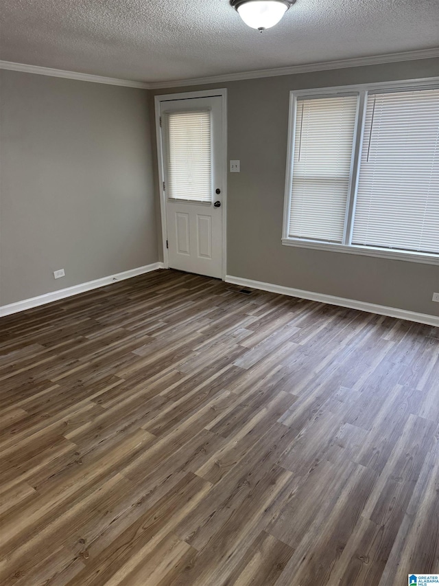 spare room with a textured ceiling, ornamental molding, dark wood-type flooring, and baseboards