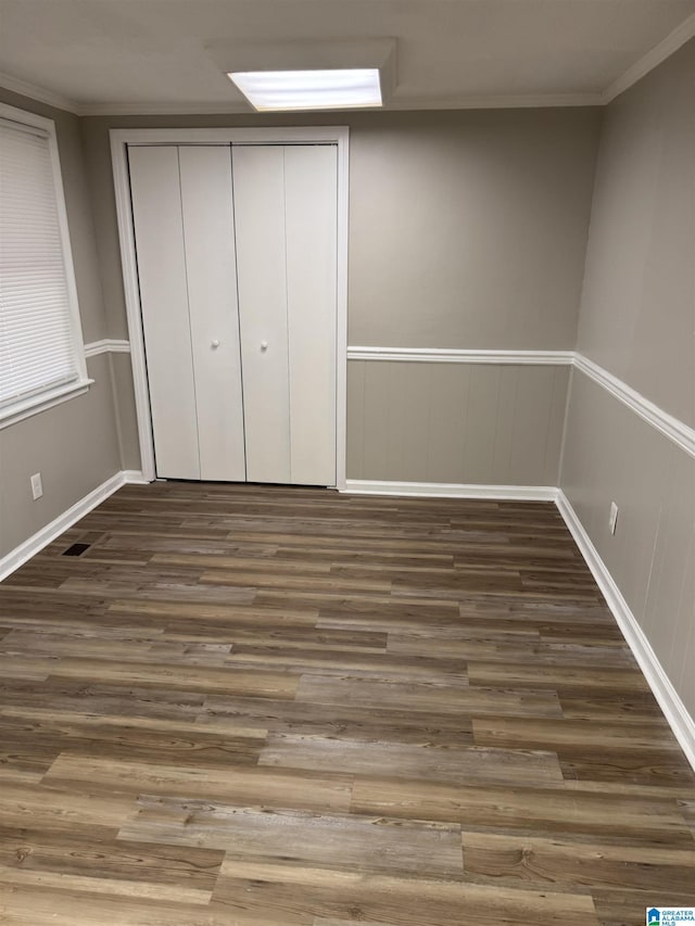 unfurnished bedroom with a wainscoted wall, dark wood-style flooring, a closet, and crown molding