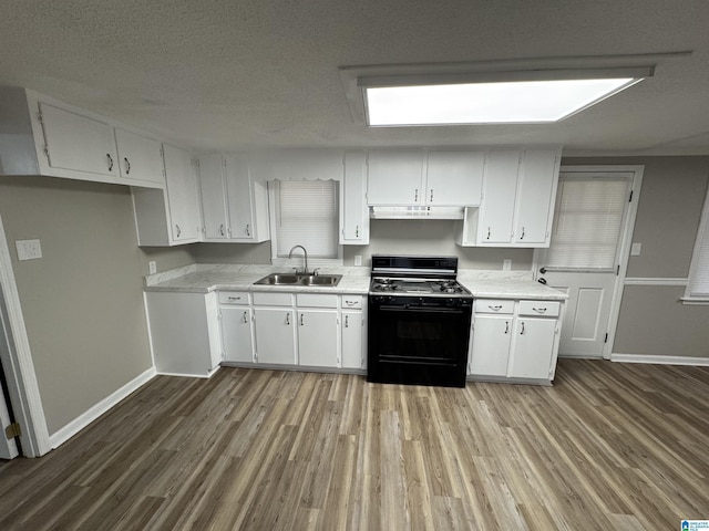 kitchen featuring black range with gas cooktop, white cabinets, light countertops, under cabinet range hood, and a sink