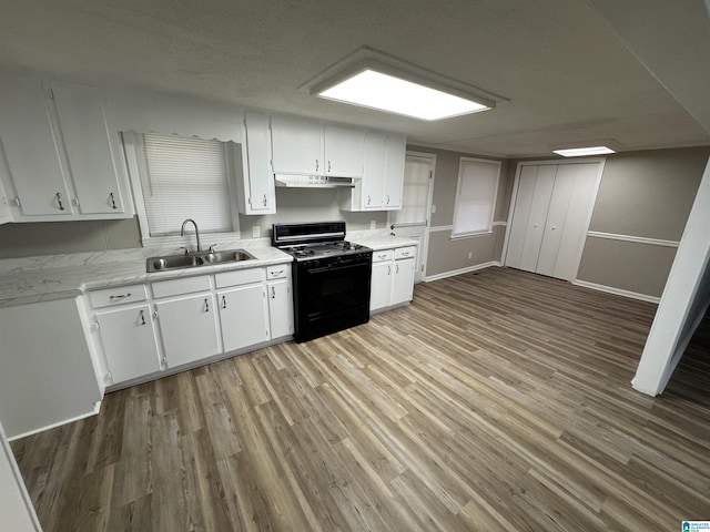 kitchen with light countertops, a sink, black gas stove, and white cabinetry