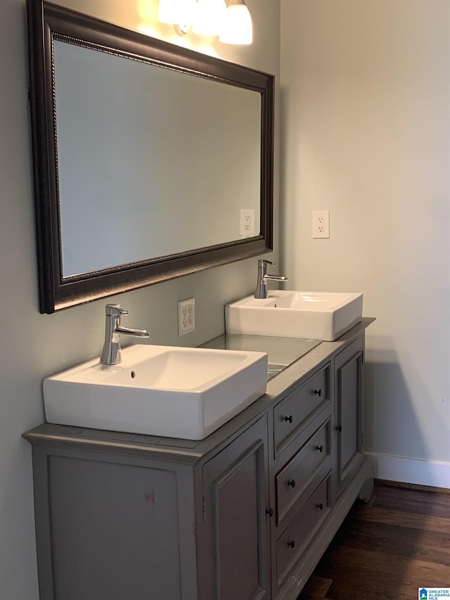 full bath featuring double vanity, wood finished floors, a sink, and baseboards