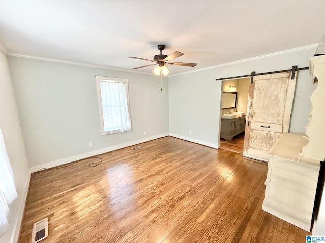 unfurnished bedroom with a barn door, baseboards, visible vents, ornamental molding, and wood finished floors