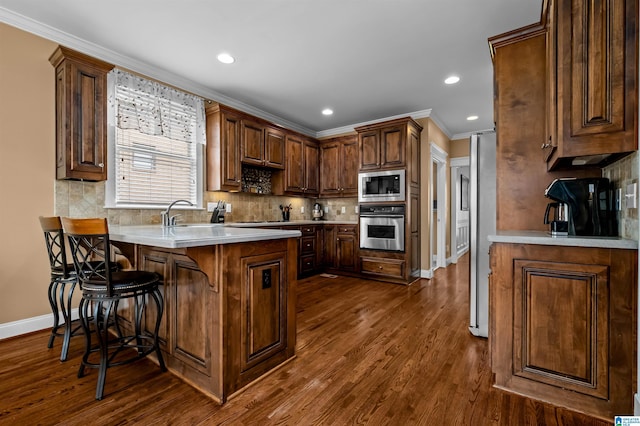 kitchen with a breakfast bar, stainless steel appliances, light countertops, ornamental molding, and a peninsula