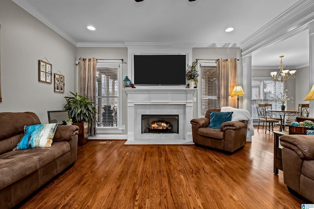 living area with a warm lit fireplace, recessed lighting, wood finished floors, ornamental molding, and an inviting chandelier