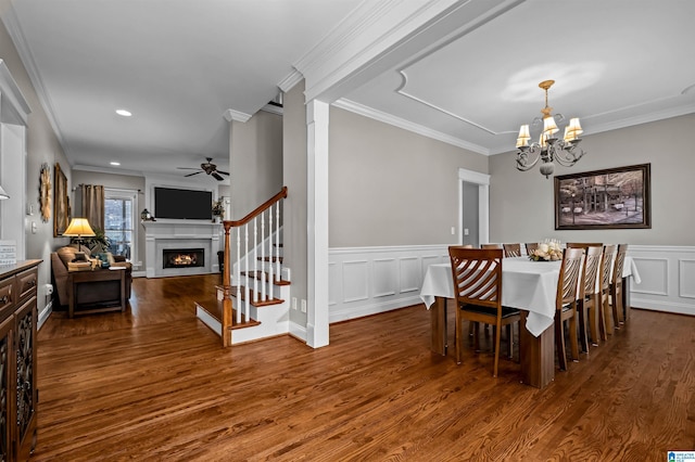 dining room with dark wood-style floors, ornamental molding, a lit fireplace, and a decorative wall