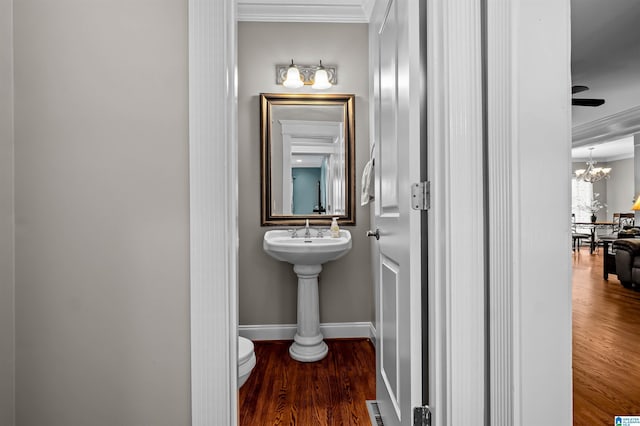 bathroom featuring baseboards, toilet, wood finished floors, crown molding, and a chandelier