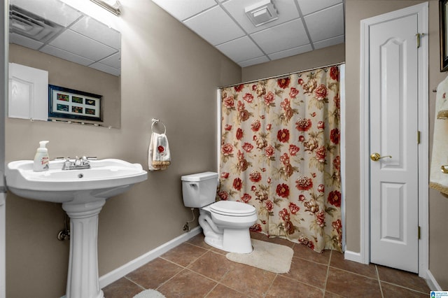 bathroom with baseboards, a drop ceiling, and tile patterned floors