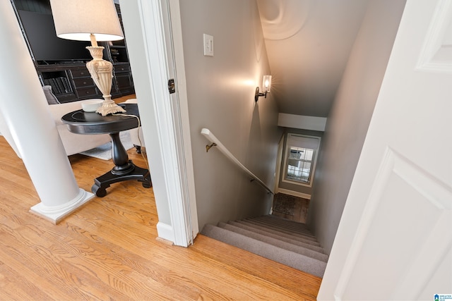 stairway with decorative columns and wood-type flooring