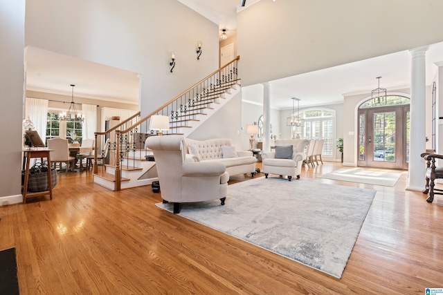 living room featuring decorative columns, ornamental molding, a notable chandelier, a towering ceiling, and light hardwood / wood-style floors