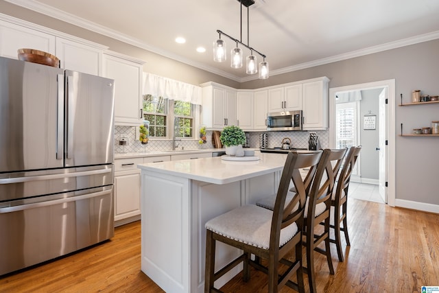 kitchen featuring a kitchen island, white cabinets, hanging light fixtures, stainless steel appliances, and crown molding