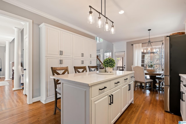 kitchen featuring a kitchen island, a breakfast bar, pendant lighting, stainless steel refrigerator, and white cabinetry