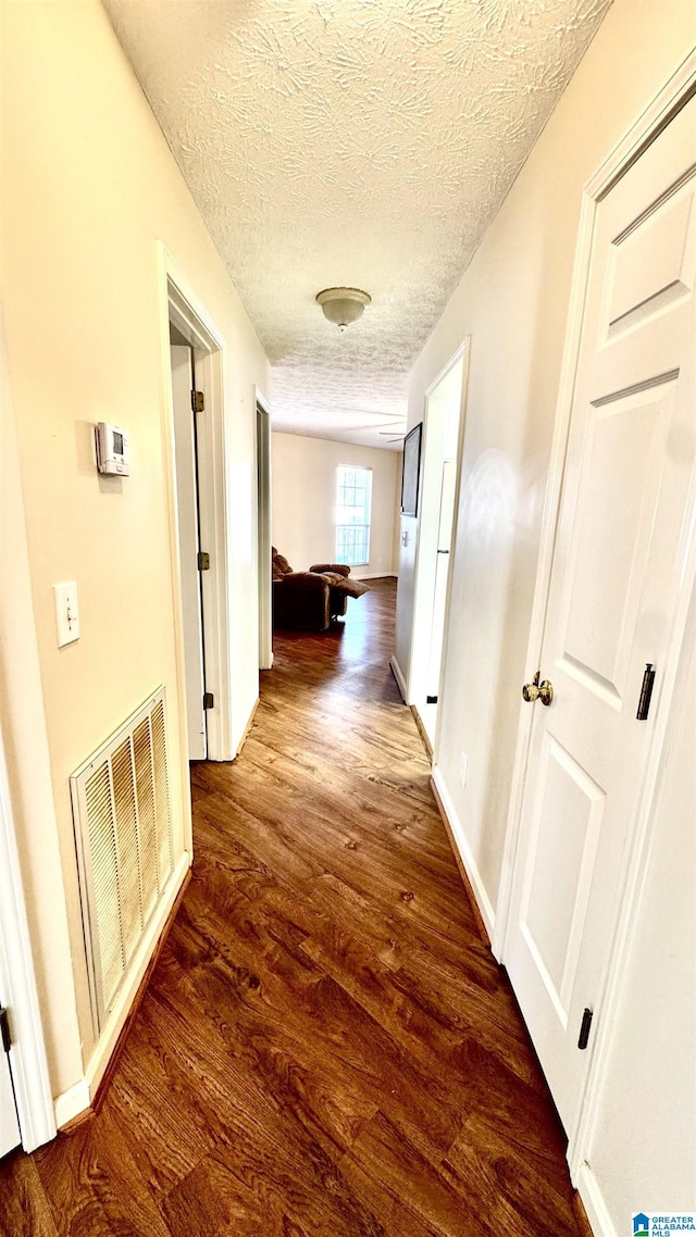 corridor with dark hardwood / wood-style floors and a textured ceiling