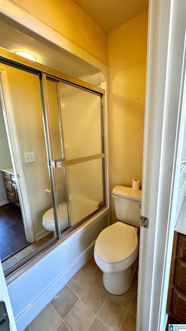 bathroom featuring tile patterned floors, toilet, and combined bath / shower with glass door