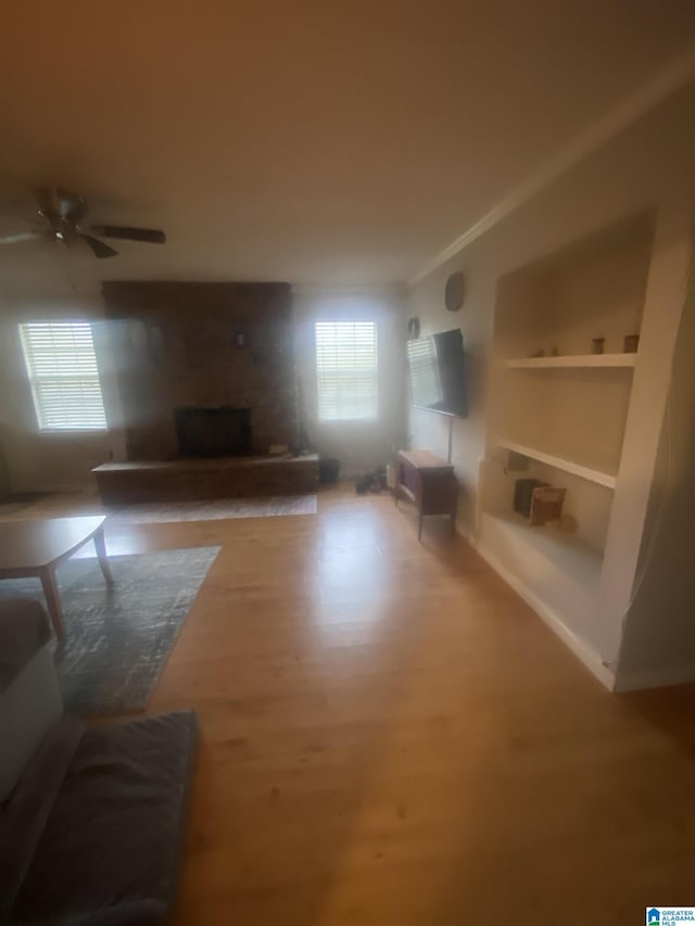 living area featuring built in shelves, a brick fireplace, a healthy amount of sunlight, and wood finished floors