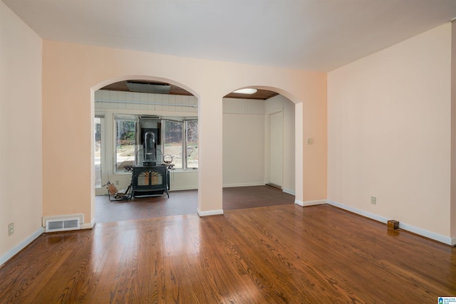 empty room with dark hardwood / wood-style flooring and a wood stove