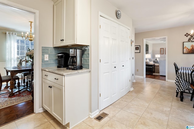 kitchen featuring light tile patterned floors, white cabinetry, light stone counters, tasteful backsplash, and a chandelier