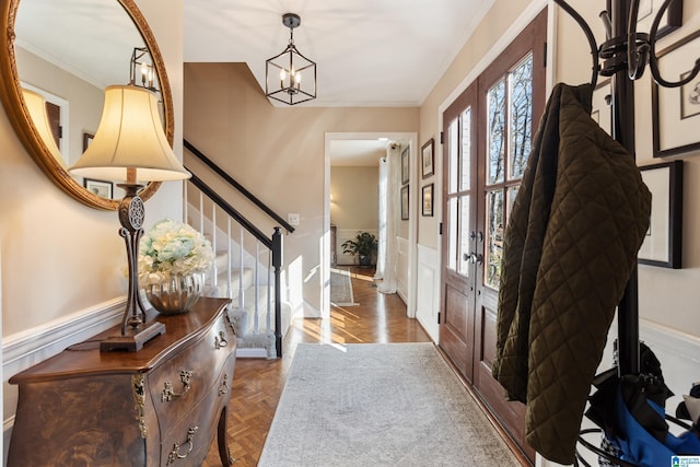 entrance foyer with dark parquet flooring, an inviting chandelier, and crown molding