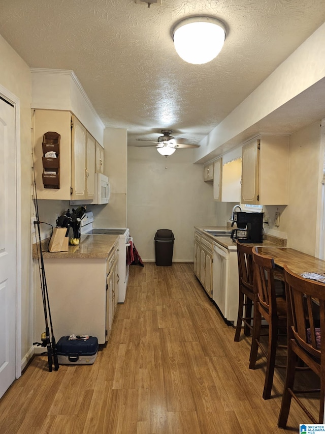 kitchen featuring sink, white appliances, cream cabinets, a textured ceiling, and light wood-type flooring