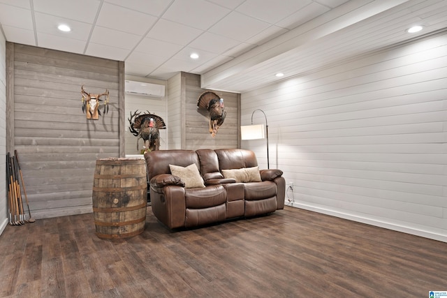 living room featuring dark wood-type flooring, a wall unit AC, wood walls, and a paneled ceiling