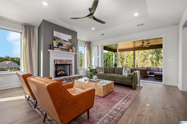 living room featuring ceiling fan, a fireplace, vaulted ceiling, and light hardwood / wood-style flooring