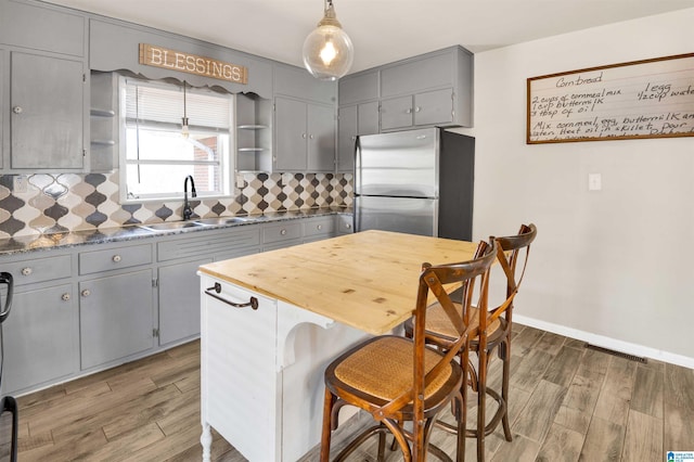 kitchen featuring sink, gray cabinets, stainless steel fridge, hanging light fixtures, and tasteful backsplash