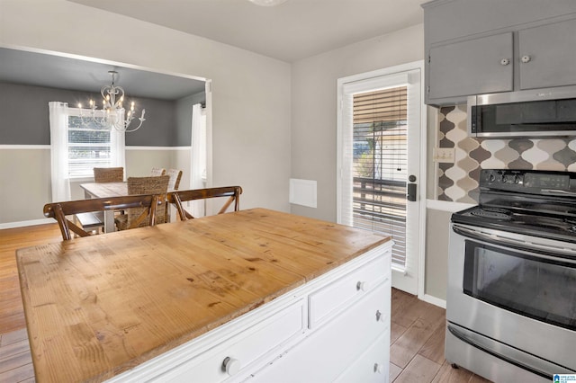 kitchen with stainless steel appliances, light hardwood / wood-style flooring, a healthy amount of sunlight, a chandelier, and pendant lighting