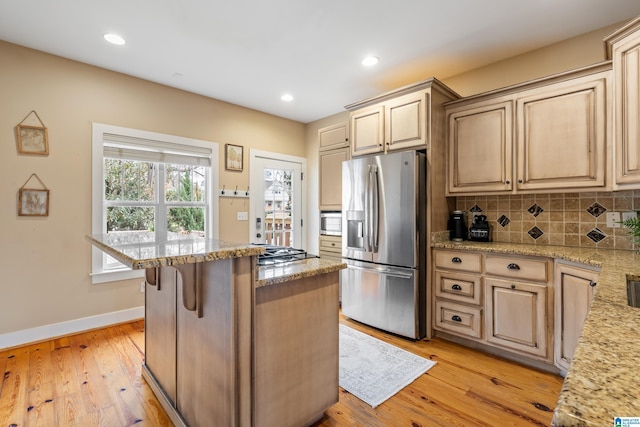 kitchen with light wood-type flooring, stainless steel appliances, light brown cabinets, and decorative backsplash