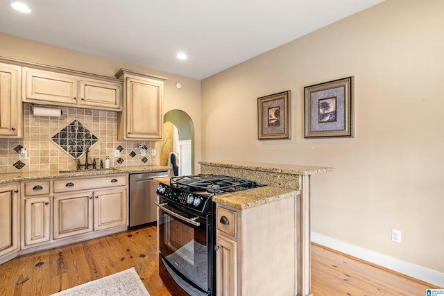 kitchen with stainless steel dishwasher, sink, black gas range oven, and light stone countertops