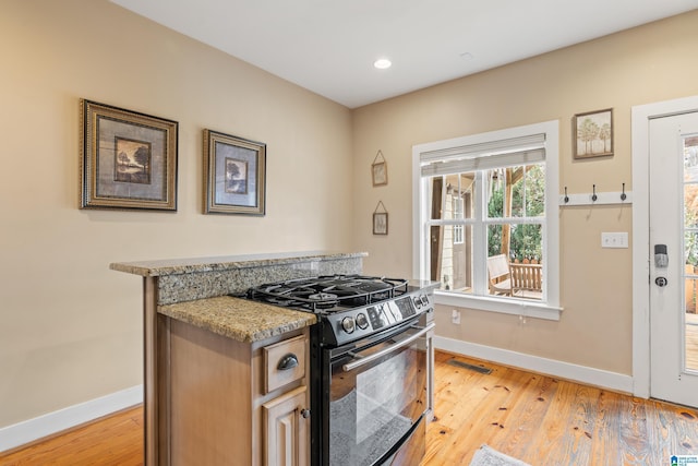 kitchen with black gas stove, light wood-type flooring, and light stone counters