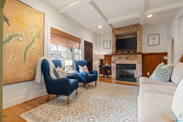 living room with beam ceiling, coffered ceiling, light wood-type flooring, and a stone fireplace