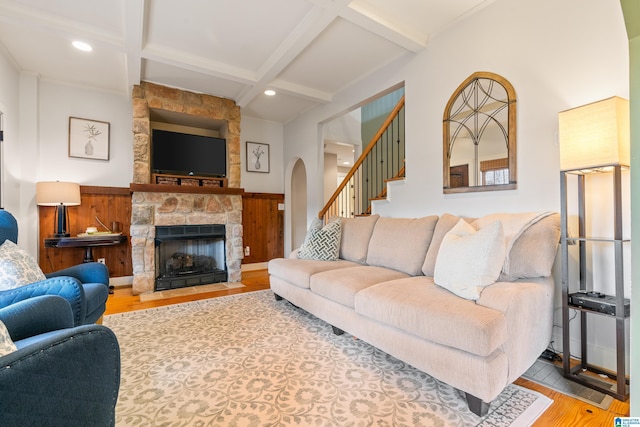 living room with beam ceiling, a stone fireplace, wood-type flooring, and coffered ceiling