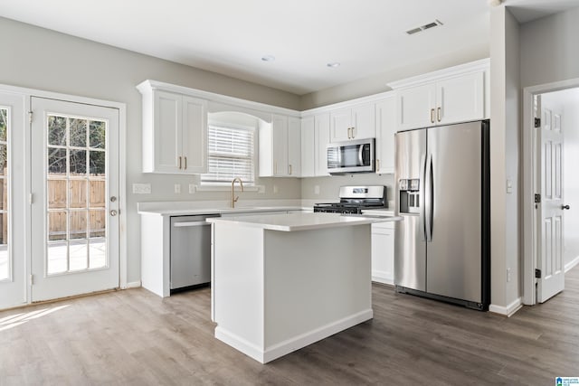 kitchen with appliances with stainless steel finishes, white cabinetry, sink, hardwood / wood-style flooring, and a center island