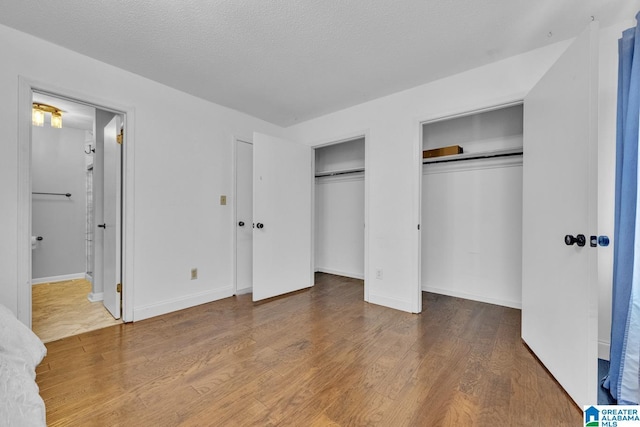 unfurnished bedroom with hardwood / wood-style floors, ensuite bath, multiple closets, and a textured ceiling