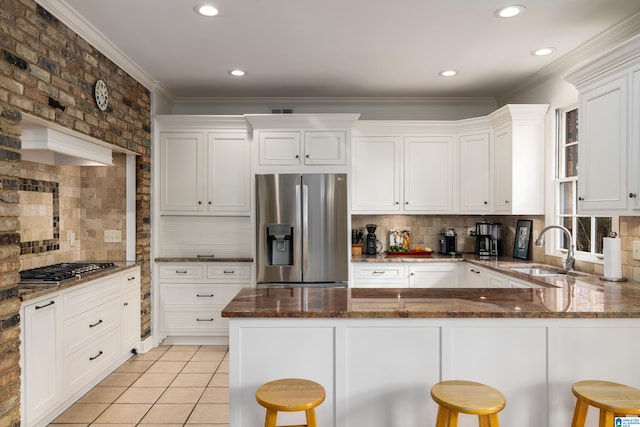 kitchen featuring appliances with stainless steel finishes, dark stone countertops, a kitchen bar, white cabinetry, and a sink