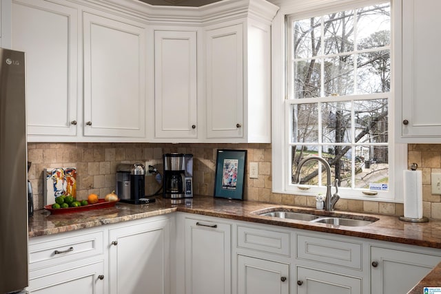 kitchen with freestanding refrigerator, backsplash, a sink, and white cabinetry