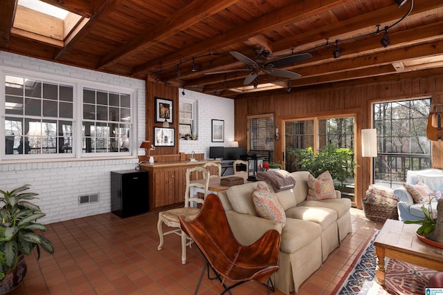 tiled living room featuring a skylight, visible vents, wood ceiling, brick wall, and beamed ceiling