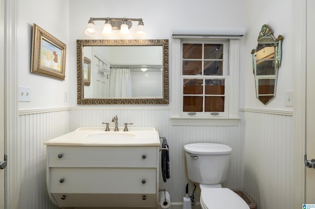 full bathroom with toilet, a shower with curtain, vanity, and wainscoting