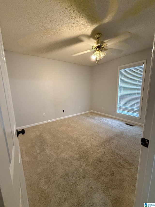 carpeted empty room with a ceiling fan, visible vents, a textured ceiling, and baseboards