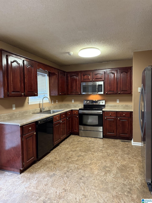 kitchen featuring light countertops, appliances with stainless steel finishes, a sink, a textured ceiling, and baseboards